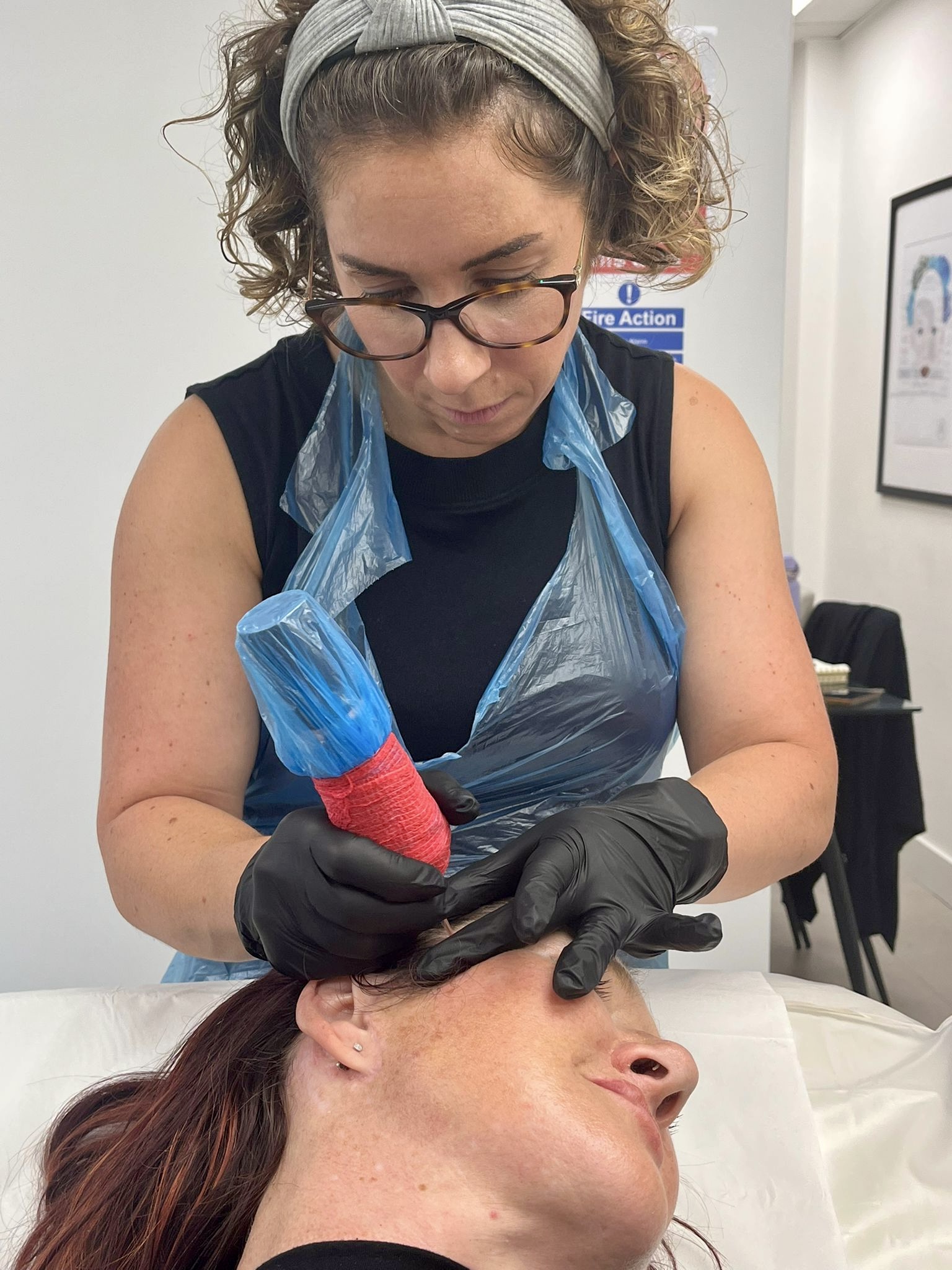 Helen in gloves and apron, working on a client's brows in the treatment room